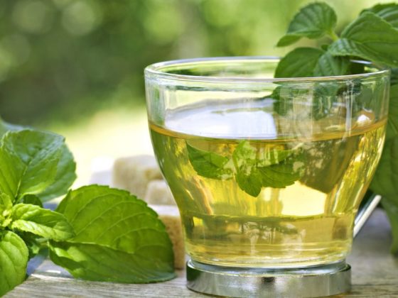 A glass of mint tea on a table covered in mint leaves